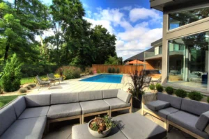 Modern backyard with pool, patio furniture, and greenery.